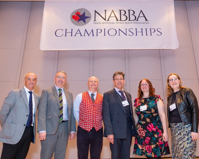 Six people posing on stage beneath the NABBA Championships banner