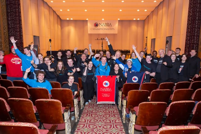 Cheering band members in a theatre aisle holding a NABBA second-place banner