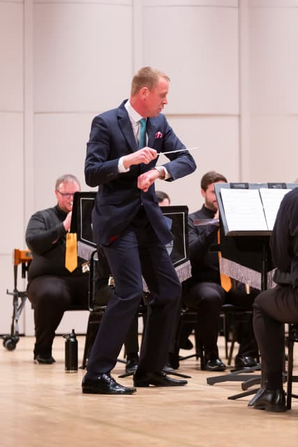 Conductor with baton leads seated brass band on a concert hall stage