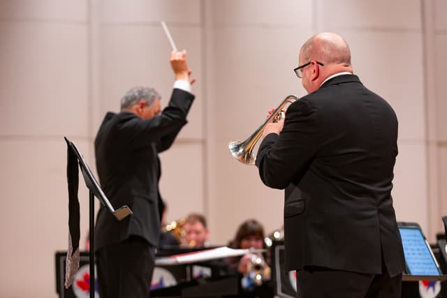Conductor with raised baton and a cornet soloist performing in front of a seated brass band