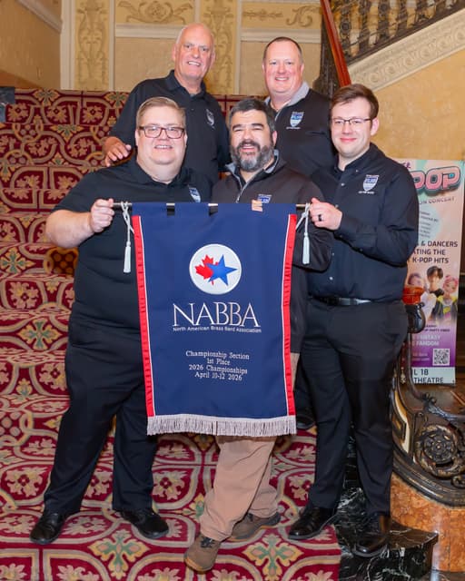 Five people on a decorative staircase holding a NABBA first place championship banner