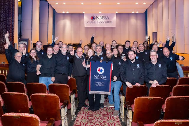 Group of band members cheering with a NABBA first place banner in a theatre