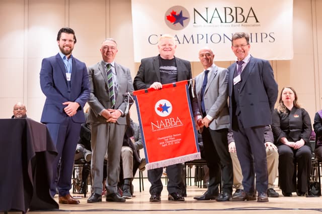 Group on stage holding a red NABBA Championship Section 2nd Place banner at the awards ceremony