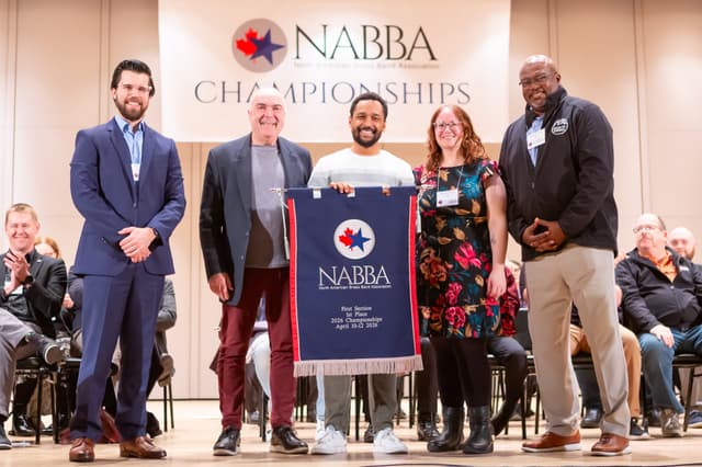 Group on stage holding a NABBA First Section 1st Place banner at the championships