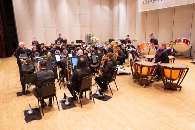 Brass band playing on stage with conductor, trombones, tubas and timpani