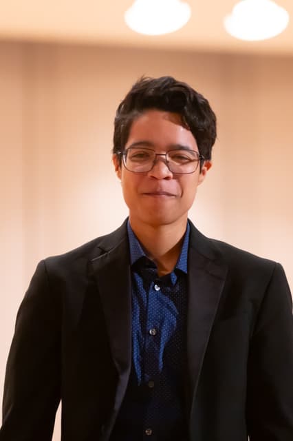 Smiling person in dark blazer and glasses in a warmly lit hall
