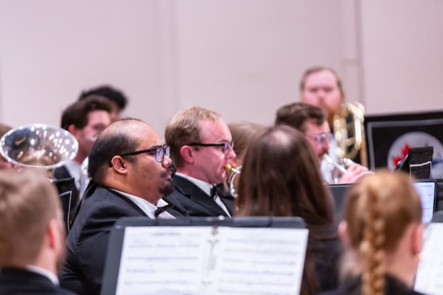 Brass band musicians in formal wear playing from sheet music on stands during a concert