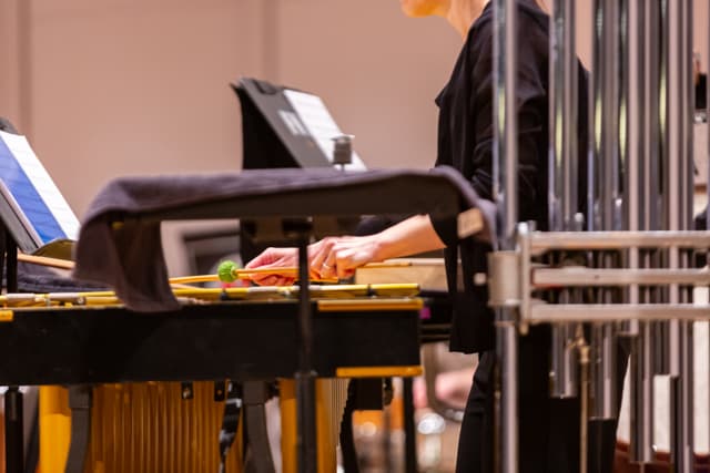 Percussionist with mallets playing a vibraphone next to tubular bells and music stands
