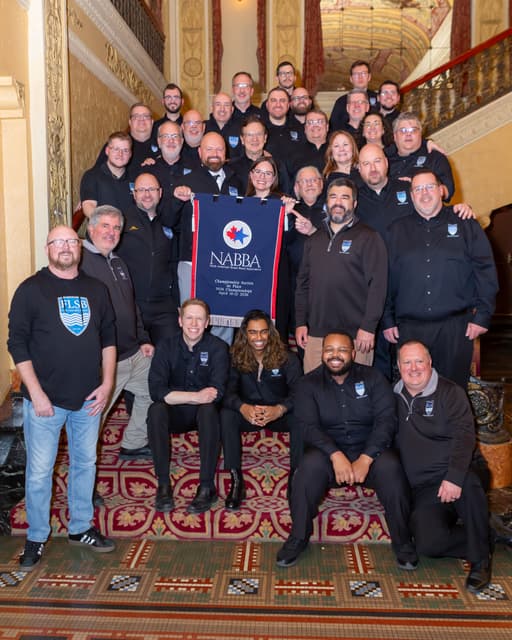 Group photo on a grand staircase holding a NABBA first place banner