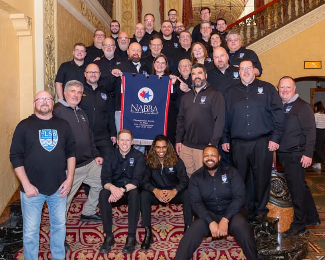 Group photo on a grand staircase holding a NABBA Championship Section first place banner