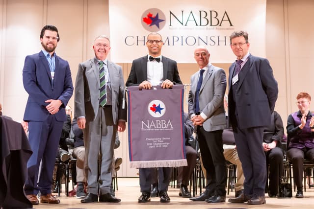 Five people on stage holding a NABBA Championship Section 3rd place banner during an awards ceremony