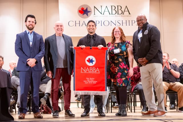 Five people on stage holding a red NABBA second place banner at the championships awards ceremony.
