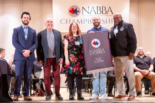 Group on stage holding a NABBA third place banner at the championships awards ceremony