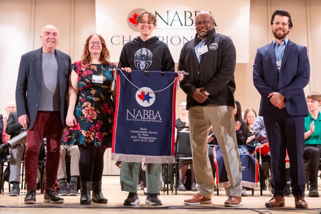 Five people on stage holding a NABBA Youth Championship Section first place banner