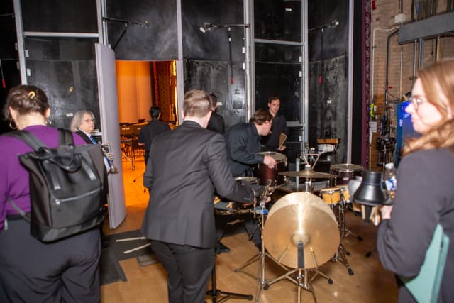 Musicians and percussion equipment backstage near an open door to the stage