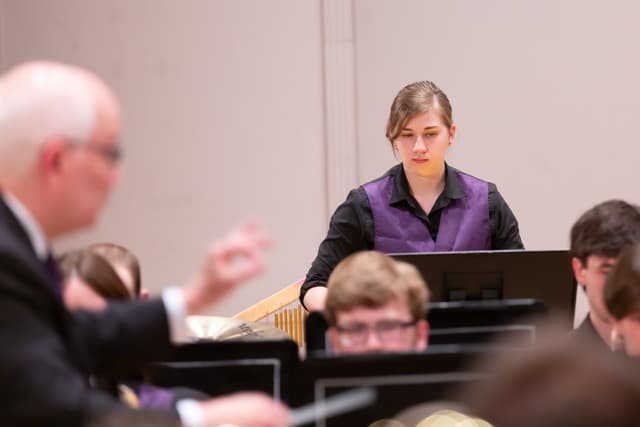 Percussionist watching the conductor, who is blurred in the foreground, during a band performance