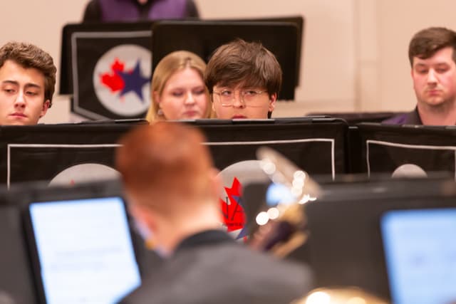 Brass band players peek over music stands with NABBA logos, a blurred player in front