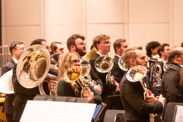 Brass band players standing with tubas and euphoniums on stage, looking attentively