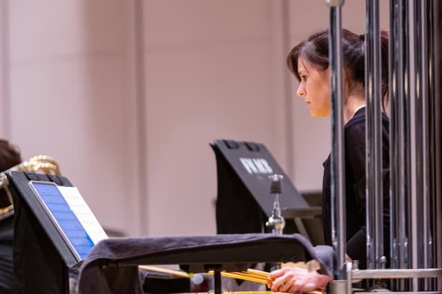 Percussionist holding mallets reads music beside tubular bells on stage