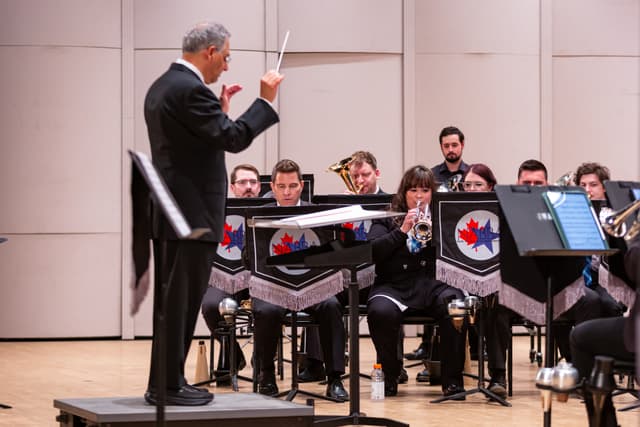 Conductor directing a seated brass band with NABBA banners on the music stands
