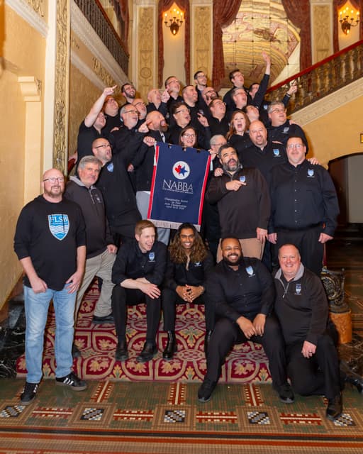 Group celebrating on a grand staircase with a NABBA first place banner