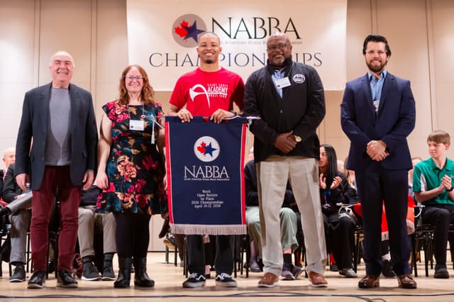 Group on stage holding a NABBA Youth Open Section first place banner at the awards ceremony