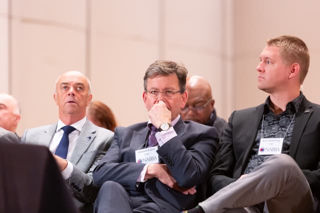 Three seated judges with NABBA badges watching a performance, one with hand over his mouth