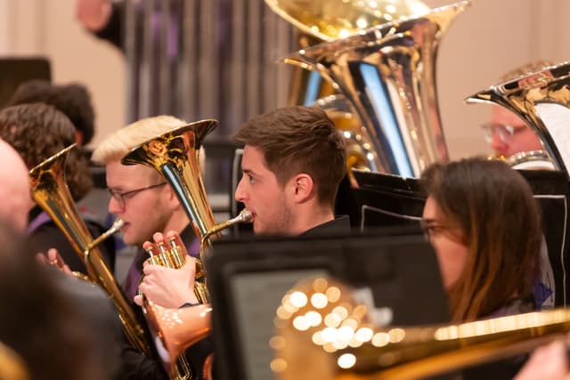 Brass band players with euphoniums and tubas performing in a warmly lit hall
