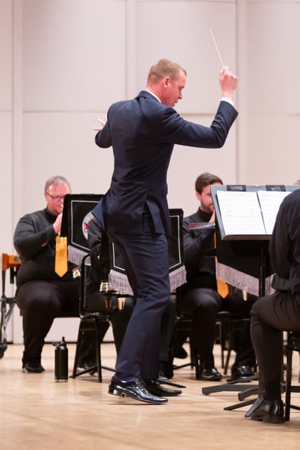 Conductor with raised baton leading a seated brass band on stage
