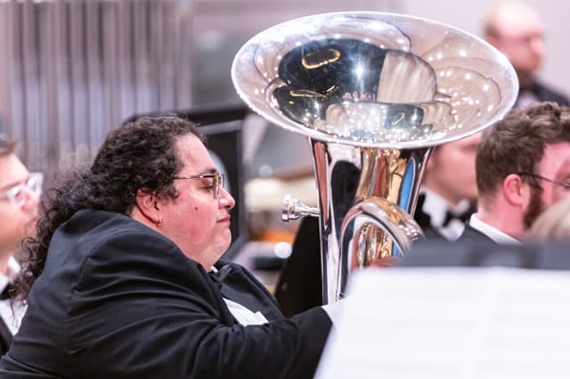 Tuba player in black concert dress beside a gleaming silver tuba bell during a performance