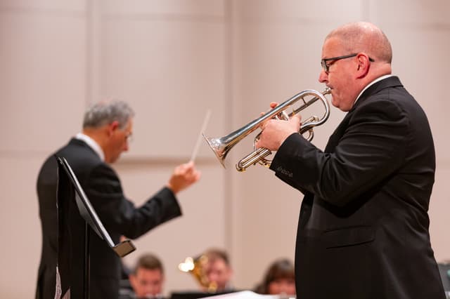 Cornet player performing in front of a conductor and seated band members on stage