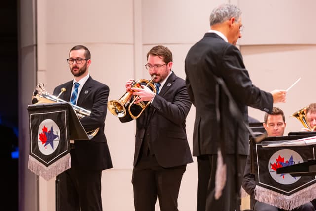 Brass band members play flugelhorn and euphonium on stage while a conductor directs.