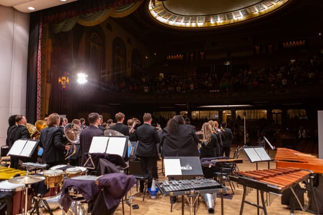 Brass band standing on stage facing applauding audience in an ornate theatre