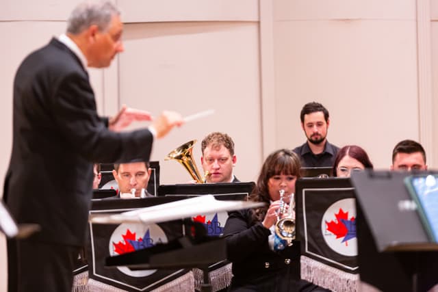 Conductor in foreground leads brass band players with NABBA banners on music stands