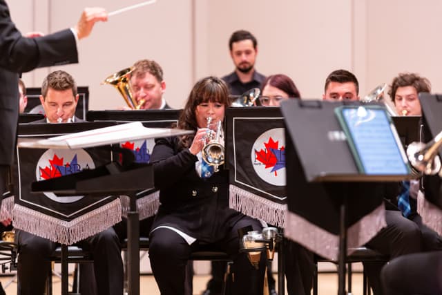 Brass band performing on stage with conductor's baton raised and a cornet player in focus