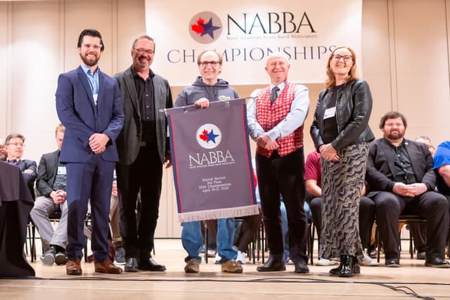 Five people on stage holding a NABBA Second Section 3rd Place banner at the awards ceremony