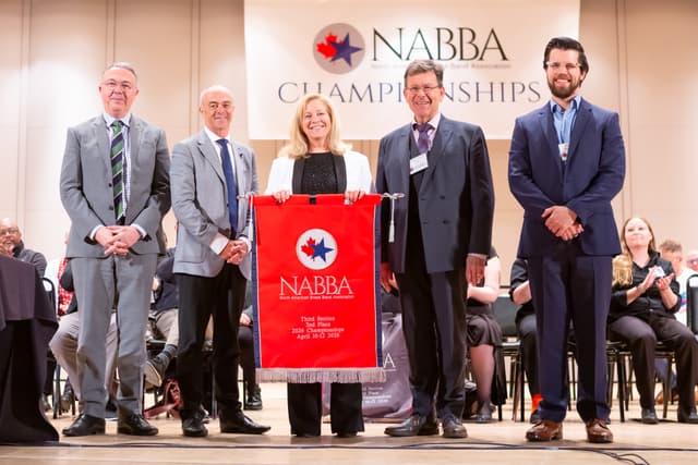 Five people on stage holding a red NABBA third section second place award banner