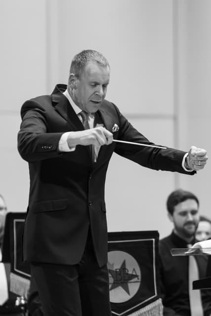 Conductor in a suit directing a brass band with a baton on stage