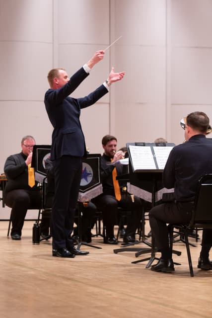 Conductor with raised baton leading a seated brass band on stage