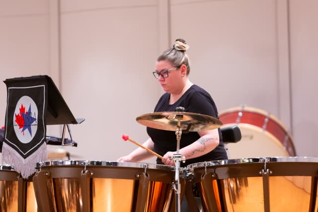Percussionist playing timpani beside a cymbal and a NABBA banner on stage