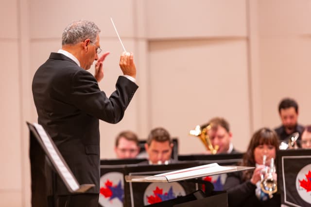 Conductor with raised baton leads a brass band on stage