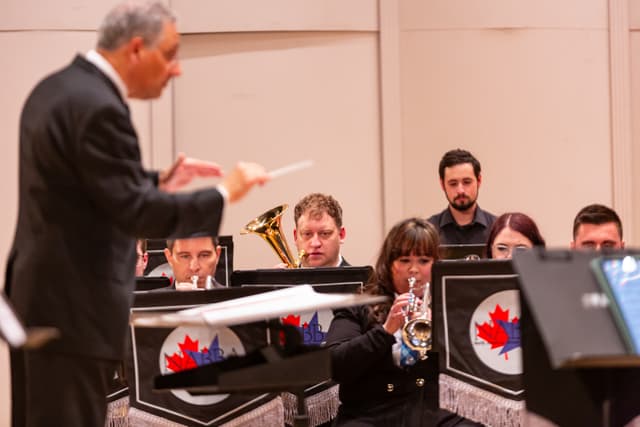 Conductor leading brass band players with cornets and euphonium behind NABBA banner stands