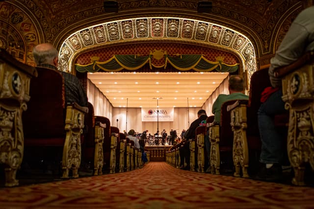 Ornate theatre aisle leading to a stage with musicians under a NABBA Championships banner