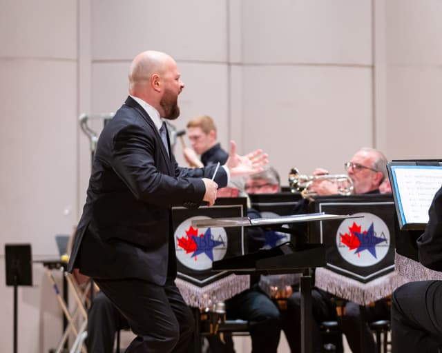 Conductor mid-gesture leading a brass band with NABBA banners on the stands