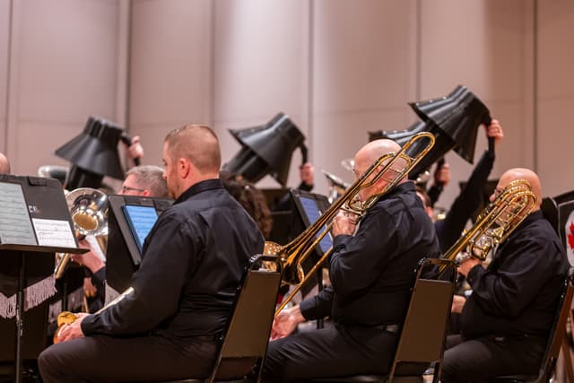 Brass band trombonists playing on stage with black bell mutes raised behind them