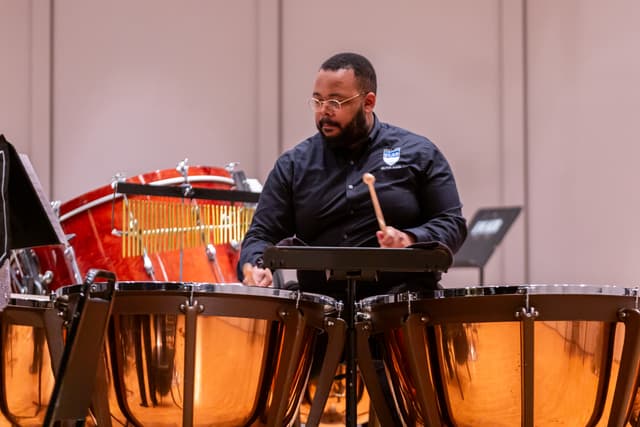 Percussionist playing copper timpani with mallets, bar chimes and a bass drum behind
