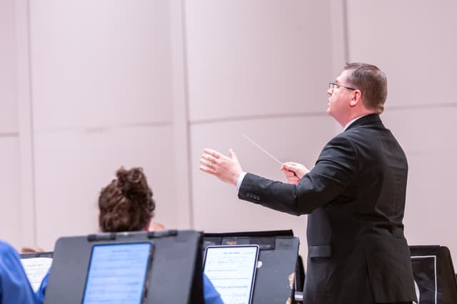Conductor with baton leading musicians who read from tablet music stands