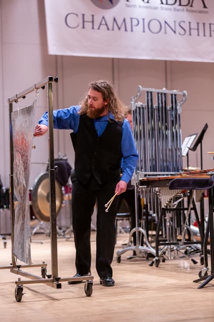 Percussionist playing a hanging metal sheet beside a marimba and gong on stage at the championship
