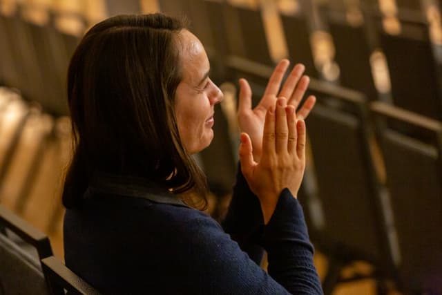 Seated audience member applauding in a theatre with rows of seats behind