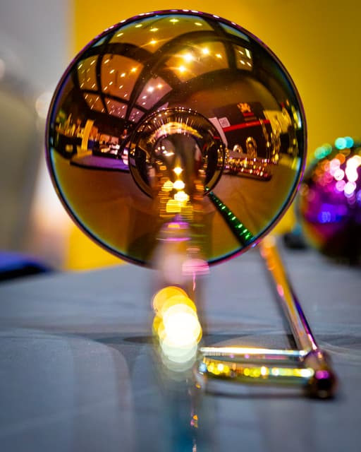Trombone bell reflecting a brightly lit hall, with colorful blurred lights behind